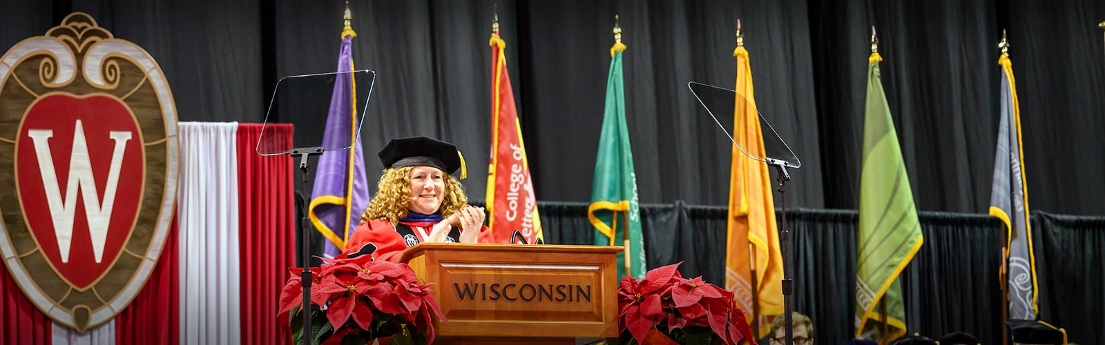 Chancellor Mnookin, in academic regalia, greets the audience during a commencement ceremony at the Kohl Center.